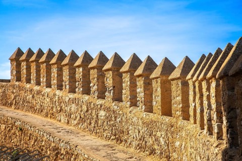 Long stone wall with regular battlements under a blue sky in sunlight, monastery with castle