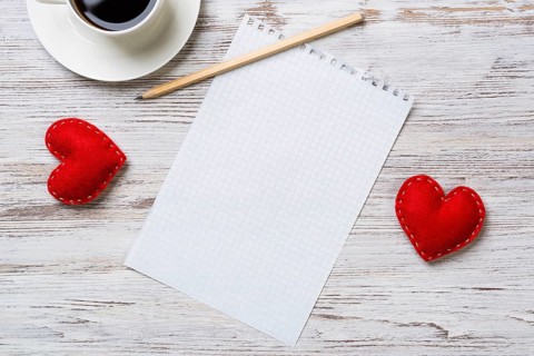 Coffee cup notepad pencil and two red hearts on wooden surface