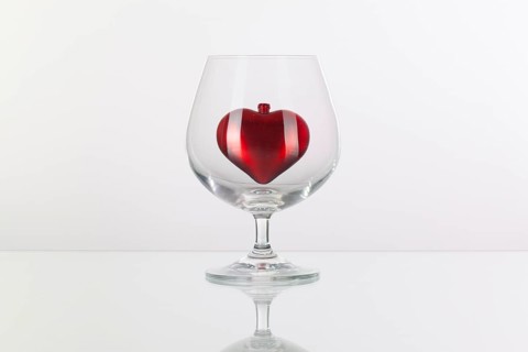 Red heart inside a glass of cognac on a glass plate