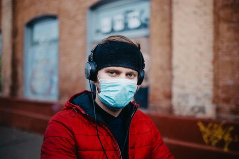 Man with a mask and headphones against a brick wall backdrop