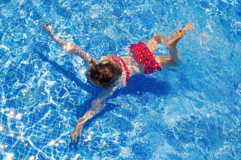 Bikini kid girl swimming on blue tiles pool in summer vacation