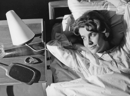 Sleep in the 1960s. A young woman lies comfortably ensconced in a bed. On the bedside table is a