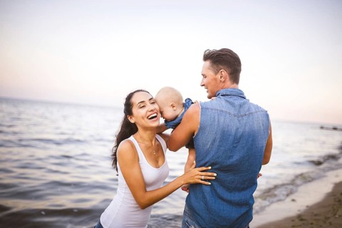 Beautiful young family on holiday with baby. The father holds the blonde girl in her arms, and the