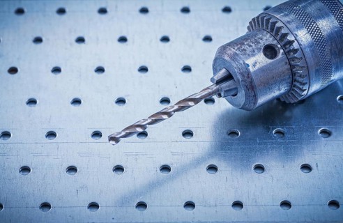 Metal drill on perforated metallic background construction concept