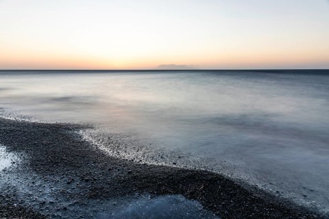 Morning atmosphere, sunrise over the sea, view from the lava beach to the island of Anafi, long