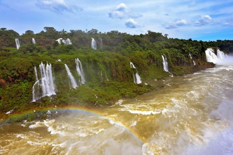 Raging and roaring water in the waterfalls of Iguazu. Turbid yellow-brown waves flow down. Above
