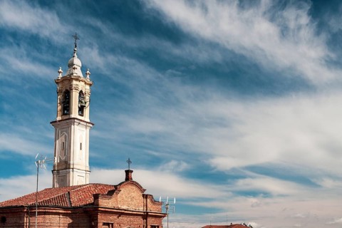 Historic church bell tower reaching out to a clear blue sky adorned with delicate clouds. Vigevano,