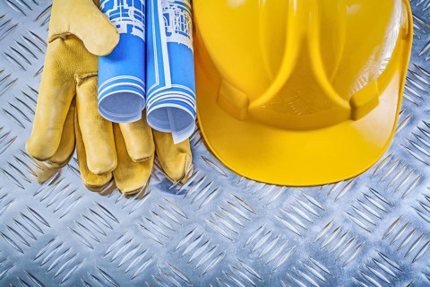 Blue engineering drawings hard hat safety gloves on corrugated metal background construction