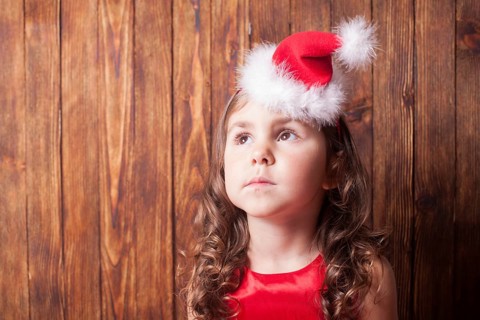 Girl in Santa hat headband sitting over wooden wall, copy space