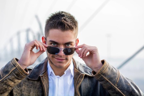 Handsome trendy young man standing on a sidewalk wearing sunglasses and a fashionable leather