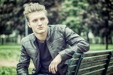 Handsome blond young man sitting on green, wooden park bench