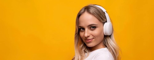 Smiling woman listening to music in white headphones on orange background with empty space