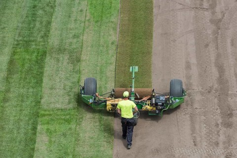 Workers laying grass in a roll on a football field at the stadium in Lubin, Poland, Europe