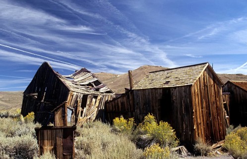 Windswept wooden houses in Bodie, collapsed by the weight of snow in winter. Colour photo,