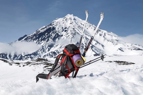 Equipment, backpack, skis and poles lie in snow on background cone of volcano on Kamchatka
