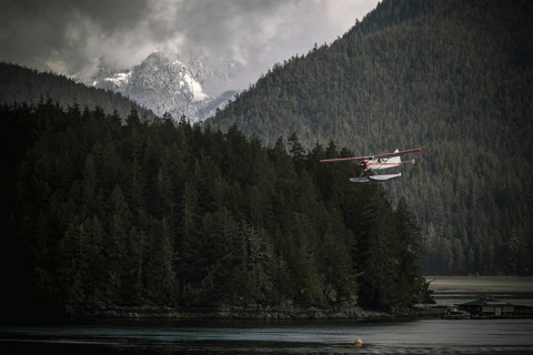 A seaplane flying over a forest and water with misty mountains in the background in Tofino on