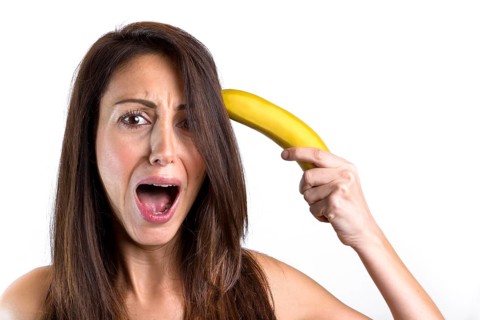 A funny portrait of a beautiful girl trying to shoot herself with a banana gun, while screaming.