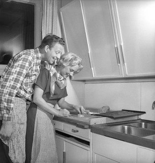 In the kitchen in the 1950s. Ayoung couple baking heart shaped gingerbread cookies for christmas.
