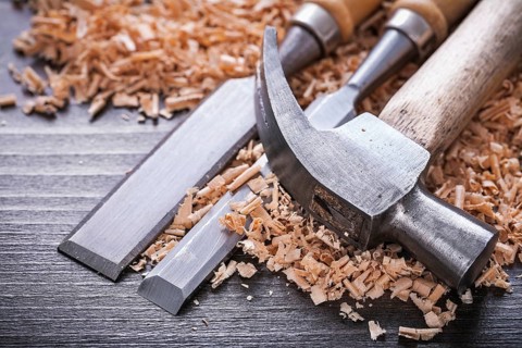 Close up of claw hammer and metal firmer chisels in wooden planning chips on vintage wood board