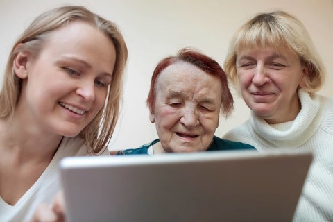 Three women of different ages smiling using a smart tablet