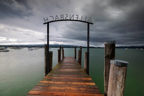 Wooden footbridge leads into a lake under a stormy sky, Allensbach, Untersee, Lake Constance,