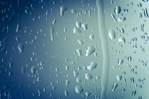 Close up of splashes of water and waterdrops running down on glass panel of bathtub in bathroom