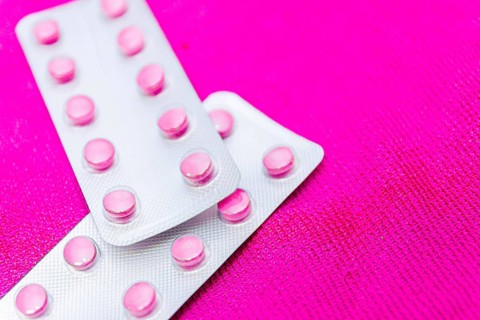 Pink pills in a blister on a pink background