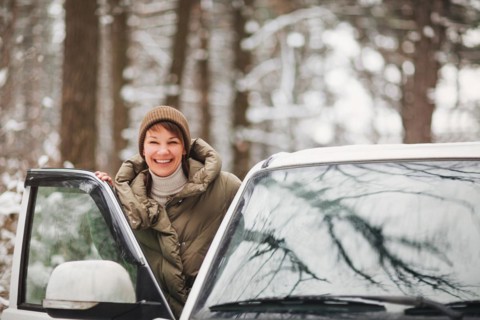 Cheerful female smiling and looking at camera while driving modern vehicle on blurred background of