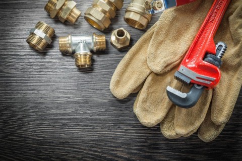Plumbing monkey wrench pipe fittings protective gloves water valve on wooden board