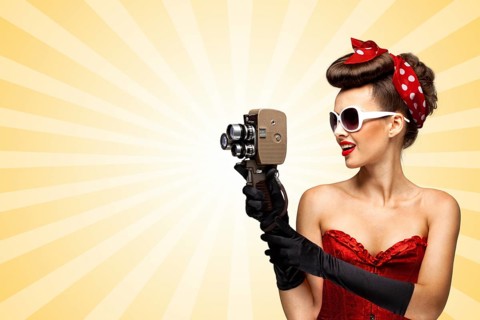 Vintage photo of glamorous pinup girl wearing a sexy red corset, shooting with an old retro cinema