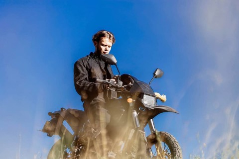 A young man in black clothing sitting on a motorcycle under a clear blue sky
