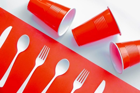 Horizontal view of single use white plastic cutlery and red plastic glass on a red and white
