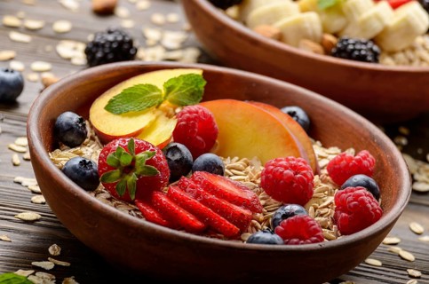 Fruit healthy muesli with peaches strawberry almonds and blackberry in clay dish on wooden kitchen