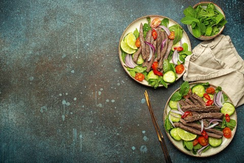 Two plates with traditional Thai beef salad with vegetables and mint top view served on rustic