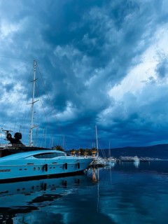 White motor yacht stands on the pier against the background of a twilight dark sky.