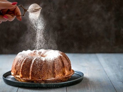 Woman's hand sprinkling icing sugar over fresh muffin cake. Powder sugar falls on fresh perfect