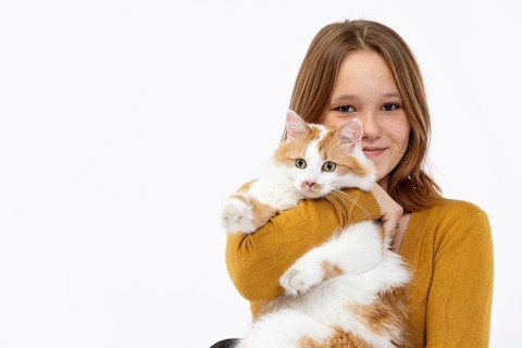 A cheerful girl lovingly holds her fluffy cat, radiating joy and warmth while wearing a cozy