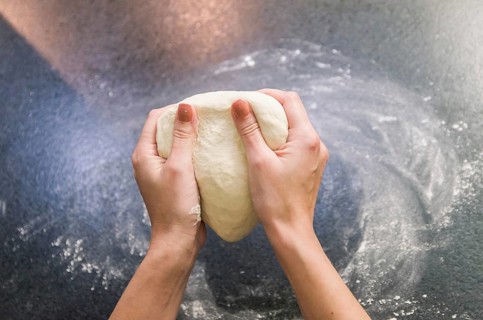 Woman preparing pizza dough on black granite table