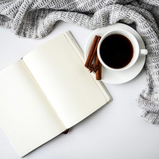 Cup of coffee with notebook cinnamon sticks and anise star on white background. Sweater around.