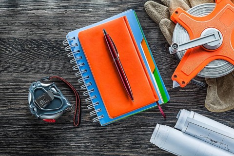 Construction drawings measuring tape protective gloves notepads pen on wood board