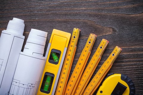 Close up view of blueprint rolls construction level tape-line and wooden meter on vintage wood