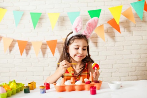 Girl with Easter bunny ears is painting colorful Easter eggs at home. Easter decorations and