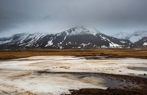 Icelandic landscape with frozen lake, mountains and meadow land covered in snow at snaefellsnes