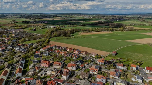 Aerial view of a neighbourhood with numerous houses and surrounding fields under a cloudy sky,