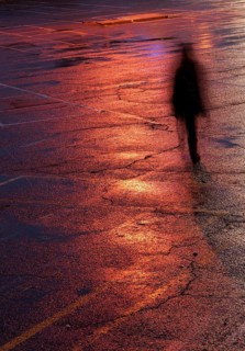 Unrecognised person walking alone in the dark under bright orange light after rain