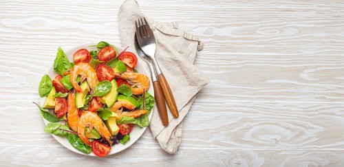 Healthy salad with grilled shrimps, avocado, cherry tomatoes and green leaves on white plate with