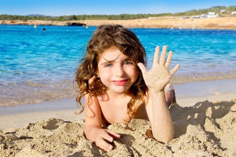 Little girl greeting hand gesture in sandy beach of Ibiza Cala Conta