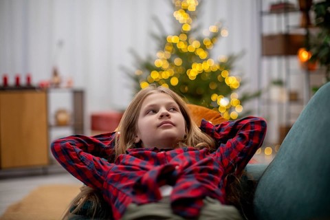 A joyful child relaxes in a cozy, warm setting, surrounded by festive decorations and glowing