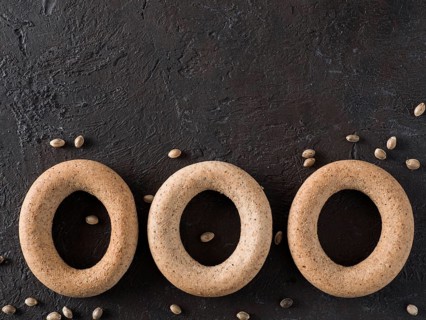 Ring-shaped cracknel with whole grain hemp seed flour and hemp seeds on black background.