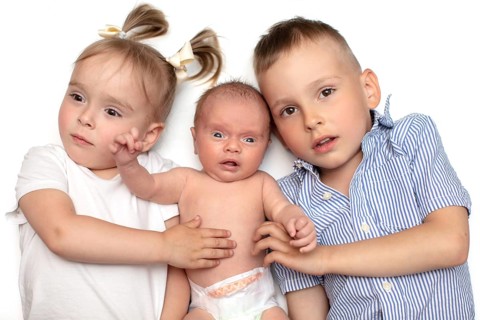 Brother and sister lying together with a newborn baby. Three small children of different ages.